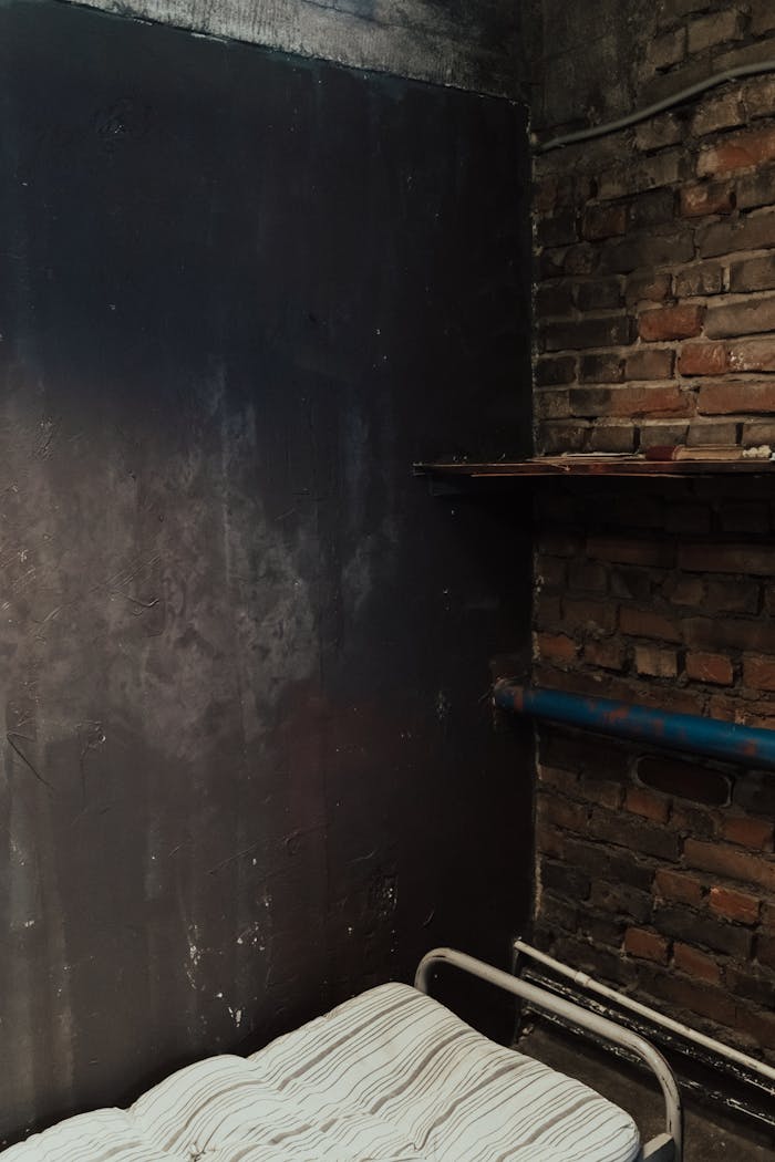 A gritty, industrial bedroom with exposed brick and metal bed, conveying isolation.